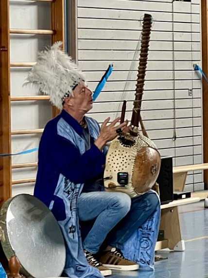 Ein Geschichtenerzähler mit Federhut musiziert auf einer gambischen Lautenharfe.